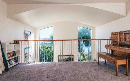 a room with a piano and a balcony with windows at Casa on Tawa, Oneroa - Be My Guest Waiheke in Oneroa