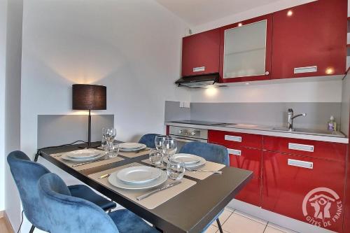 une cuisine avec une table, des chaises et des armoires rouges dans l'établissement Face a tome, à Perros-Guirec