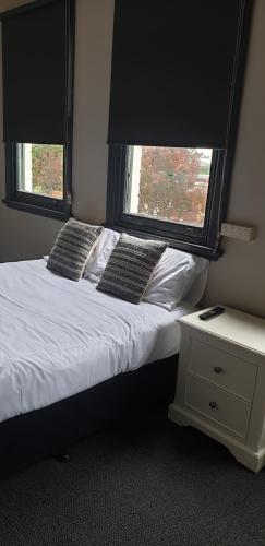a bedroom with a bed with two pillows and two windows at The Court House Hotel Narromine in Narromine