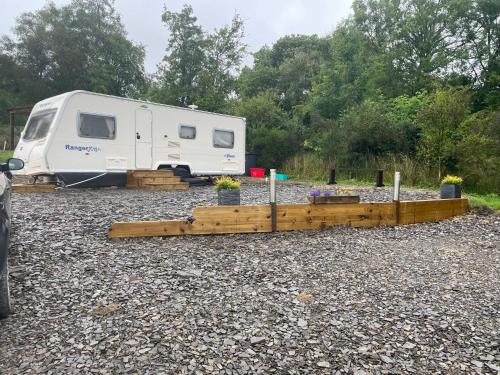 a white camper parked in a gravel area with trees at Pantyronen tourer holidays in Llanbadarn-fynydd