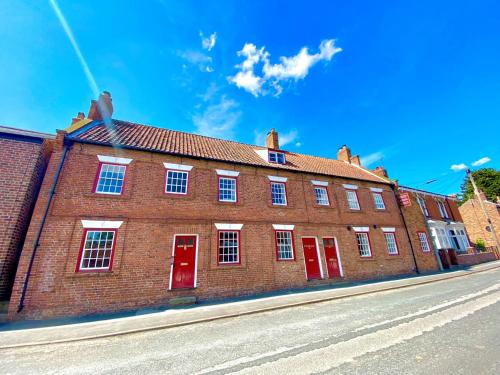 a large brick building with red doors on a street at Papist Hall Cottages in Barrow upon Humber