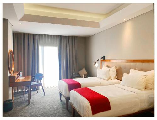 a hotel room with two beds and a desk at Famvida Hotel Lubuklinggau in Lubuklinggau
