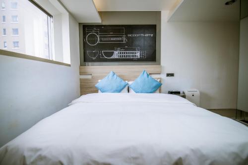 a bedroom with a white bed with blue pillows at CHECK inn Taichung Liming in Taichung