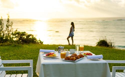 Uma mesa com comida e uma mulher caminhando à beira-mar. em Diamonds Leisure Beach & Golf Resort em Praia de Diani