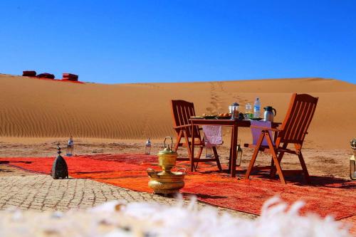 a table and two chairs in a desert with a fire hydrant at Sahara Elegance Camp in Merzouga