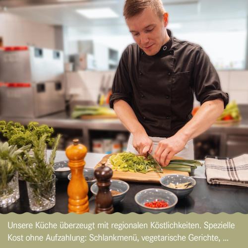 a man in a kitchen preparing food on a cutting board at Gesundhotel Bad Reuthe in Vorderreuthe