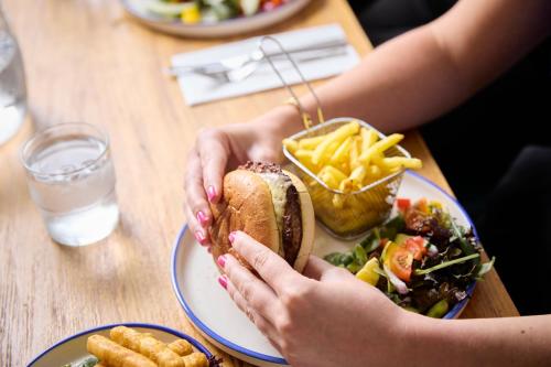 a person holding a sandwich and french fries on a table at The Lodge Hotel in Newbury