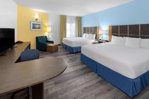 a hotel room with two beds and a table and a tv at Days Inn & Suites by Wyndham Lubbock Medical Center in Lubbock