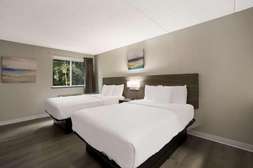 two beds in a hotel room with white sheets at Suburban Studios Milwaukee Airport in Milwaukee