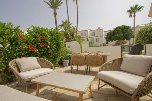 a patio with chairs and tables and palm trees at Marina de Casares Beach House in San Luis de Sabinillas