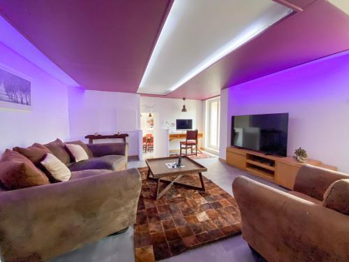 - un salon avec des murs violets, un canapé et une télévision dans l'établissement La grange en pierre - chic & piscine privée, à Queyssac