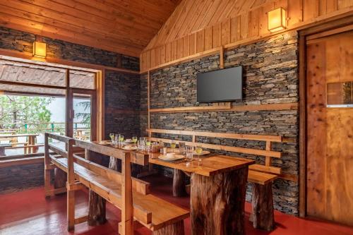 a dining room with a table and a tv on a brick wall at Alaya Stays Cottage with Tree House - Suro Woodbine Chalet in Shogi