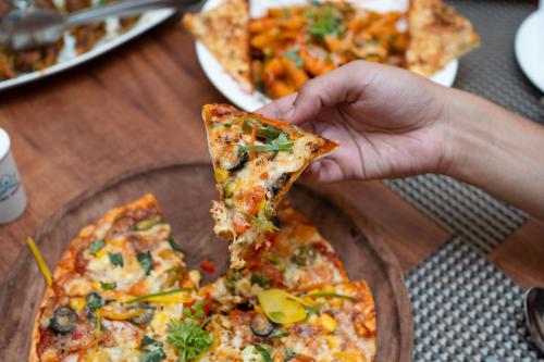 a person holding a slice of pizza on a table at Indira Nikunj Rubystone Exotic in Rishīkesh