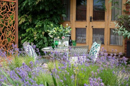 a table and chairs in a garden with purple flowers at The Clock Tower & Dairy - Two x 2 Bed Barns with Indoor Pool in Checkendon