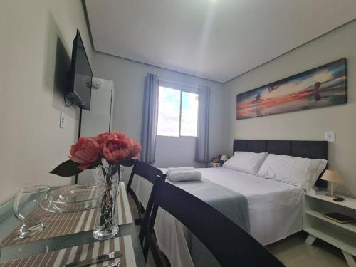 a bedroom with a bed and a table with a vase of flowers at Kitnet304 centro,c linda vista janela, tv smart in Montes Claros