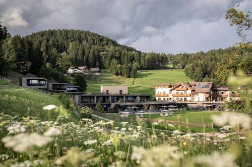 a village with a house and a field of flowers at Hotel Viertler in Avelengo