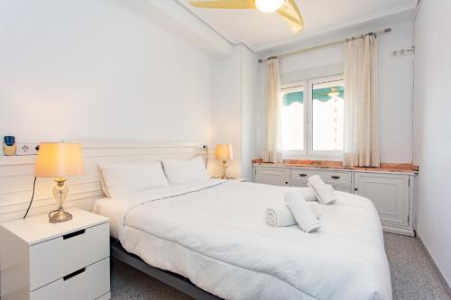 two beds in a white bedroom with a window at Cullera Horizon Apartment in Cullera