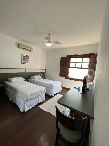 a room with two beds and a table and a desk at Hotel Fita Azul in Ilhabela