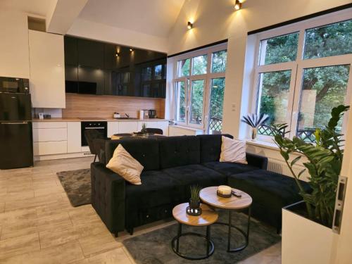 a living room with a black couch and a kitchen at Wyjątkowy Apartament w Miliczu in Milicz