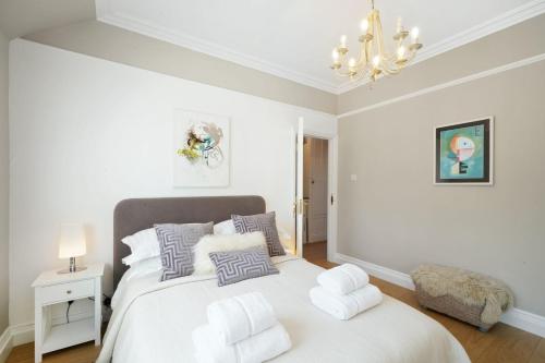 a white bedroom with a bed with pillows and a chandelier at Hidden Gem in Finchley