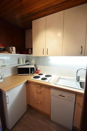 La cuisine est équipée de placards blancs, d'une cuisinière et d'un évier. dans l'établissement Résidence Le Makalu - Studio divisible 4/5 pers - LE MAKALU - PLAGNE CENTRE MAE-8534, à Aime La Plagne
