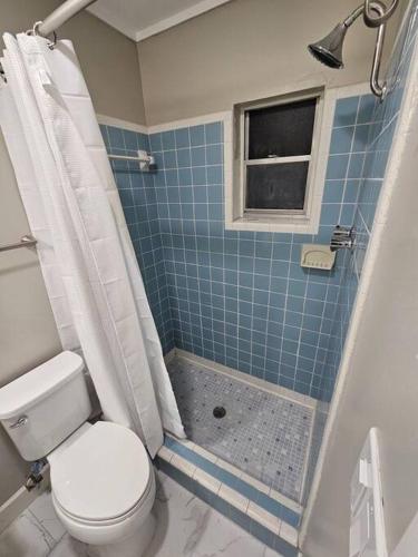 a bathroom with a toilet and a blue tiled shower at Midtown Marvel Reinvented with Contemporary Charm in Gainesville