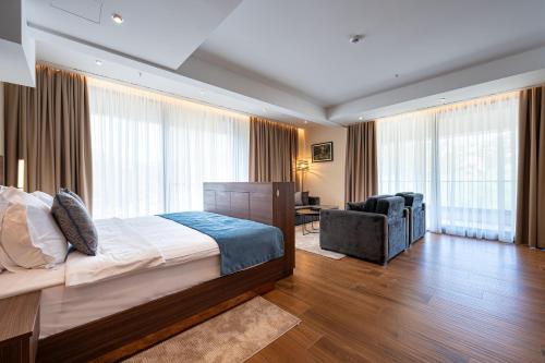 a bedroom with a bed and a chair and windows at Hotel De‘Andros Virpazar in Virpazar