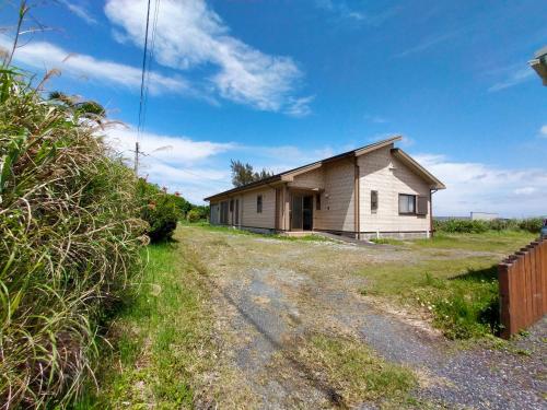 a small house on a dirt road next to a field at 奄美ゲストハウス宇宿サンライズビーチ in Amami