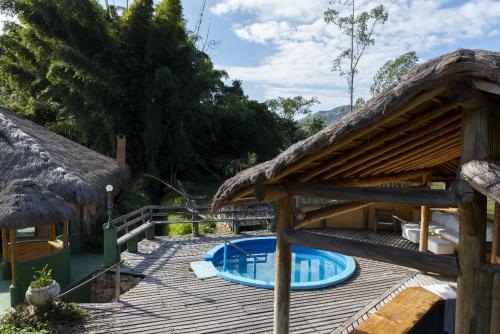 a deck with a swimming pool and a thatch roof at Hotel Fazenda Pedra Selada Rural in Visconde De Maua