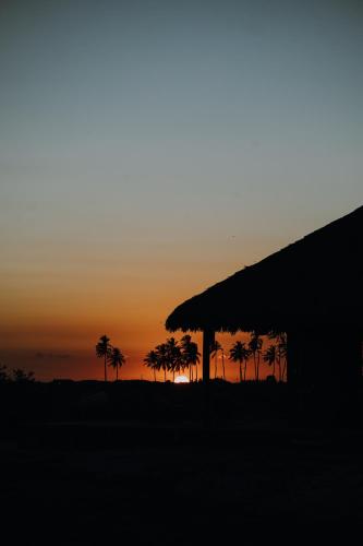 a sunset with palm trees in front of a building at Vila Ronquinha - Arpoador in Tutóia