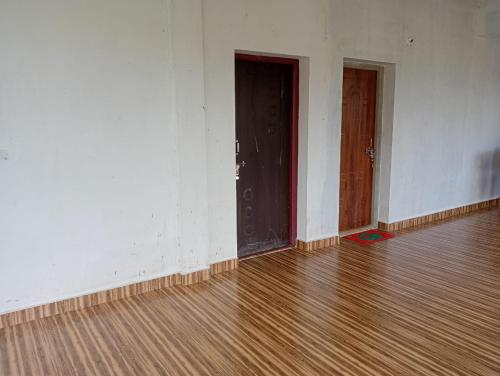 an empty room with two doors and a wooden floor at Vamoose Suyoga Homestay Kudremukh in Kalasa