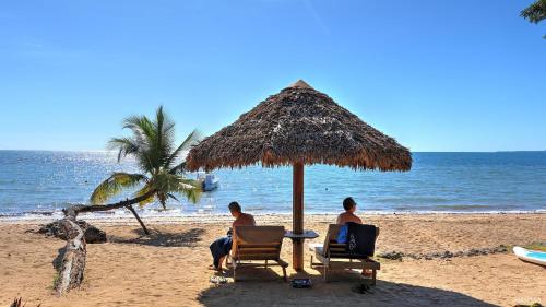 two men sitting in chairs under an umbrella on the beach at Manga Soa Lodge in Fascène - Befefika