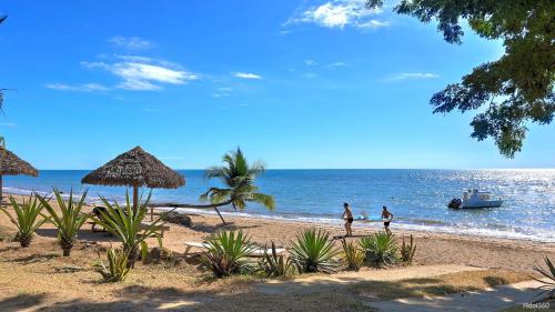 two people walking on a beach with a boat in the water at Manga Soa Lodge in Fascène - Befefika