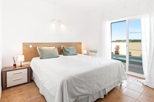 a white bedroom with a large bed and a window at Vila Agora Luz in Luz