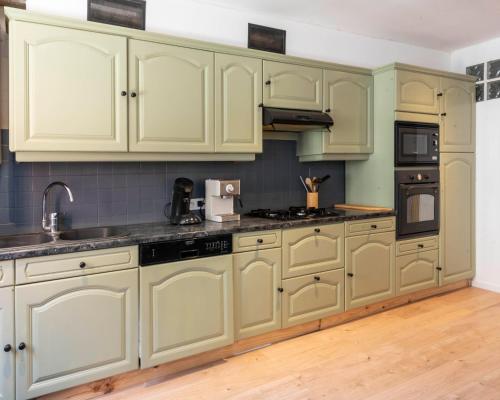 La cuisine est équipée de placards verts, d'un évier et d'une cuisinière. dans l'établissement Agréable maison de ville, à Vincelles
