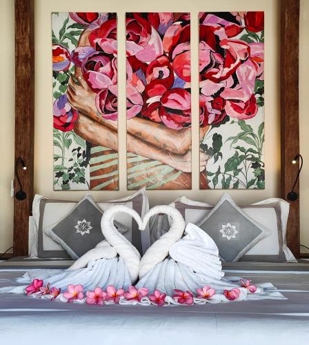 two white swans sitting on a bed in front of a painting at Kaleydo Villas in Gili Trawangan