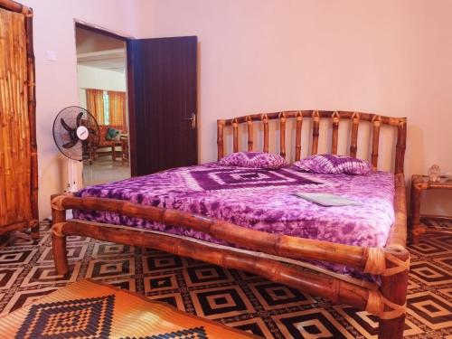 a bedroom with a wooden bed with a purple comforter at Senegambia Birding Lodge - Full board - Bird Photohide in Mandinari