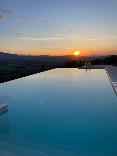 two people standing on the edge of a swimming pool at sunset at Casa Ripa North in Cupramontana