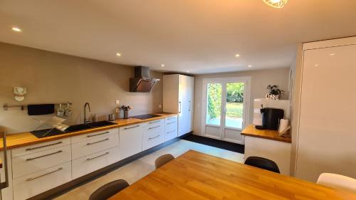 une cuisine avec des armoires blanches et une table en bois dans l'établissement La Maison du Bord du Lac, à La Chevrolière