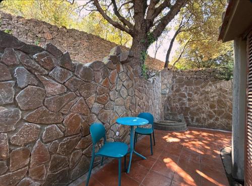 a patio with blue chairs and a stone wall at Villa Velta Sea Sunset in Porto Santo Stefano