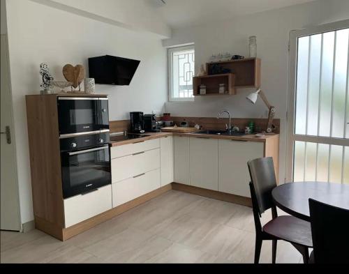 une cuisine avec des placards blancs et une table avec un four noir dans l'établissement La Maison des Pins, à Barbâtre