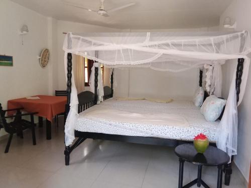 a bed with a canopy in a room with a table at Ibisbird Beach Bungalows, Sport, Spa and Restaurant in Tangalle