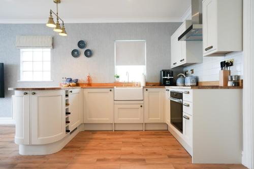 a kitchen with white cabinets and a wooden floor at Fabulous 3-bedroom home across St Michaels Mount in Marazion