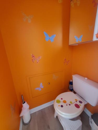 une salle de bains orange avec des toilettes et des papillons sur le mur. dans l'établissement Appartement studio bord de mer, au Cap d'Agde