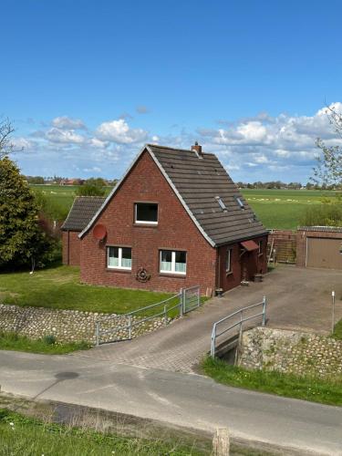 a red brick house with a fence next to a road at Ferienhaus-DeichBrand in Friedrichskoog