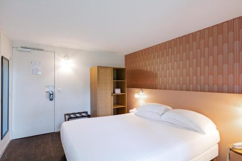a bedroom with a white bed with a wooden headboard at Eden Park Hotel Restaurant in Pont-lʼÉvêque