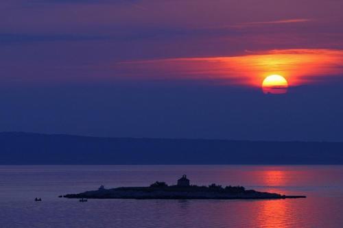a sunset over a small island in the water at Apartments Villa Mimi in Višnjan