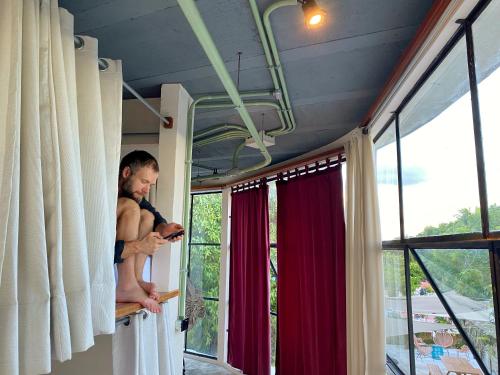 a man holding a baby in a room with windows at Elmar Hostel in Bacalar