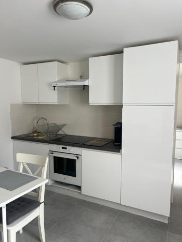 une cuisine avec des armoires blanches, une table et une cuisinière dans l'établissement Appartement gris moderne Paris et aéroport Orly, à Thiais