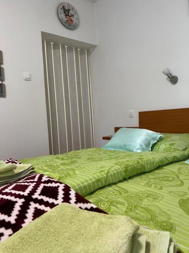 a bedroom with a green bed with a clock on the wall at Szahara Vendégház in Kerekegyháza